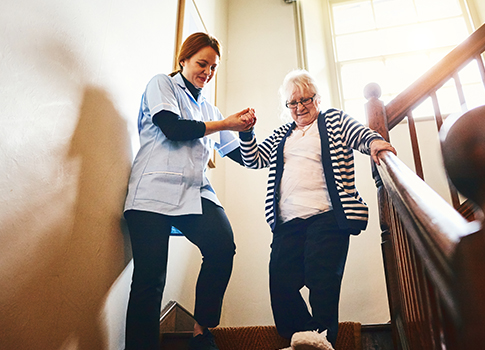 Nurse helping elderly lady down the stairs at a care home