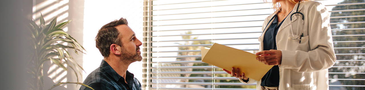 Man sitting down in doctors office listening to doctor telling him about delays in his cancer treatment