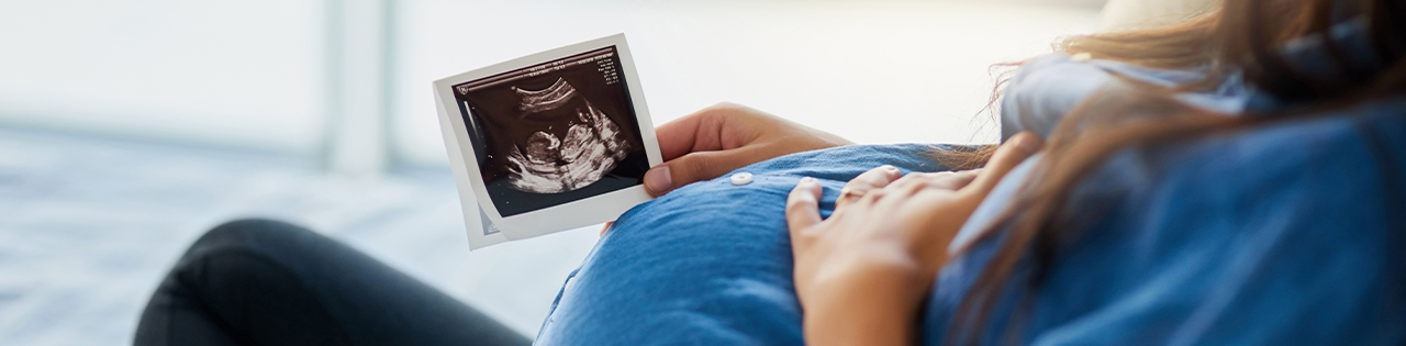 pregnant woman sitting down looking at photograph of her unborn child
