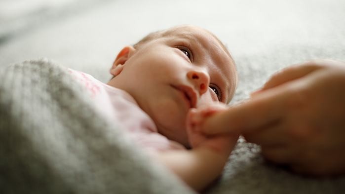 Newborn baby in cot holding mum's finger