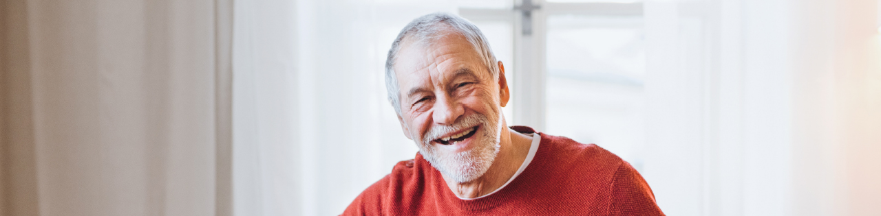 Elderly man wearing a red jumper smiling despite suffering from brain injury