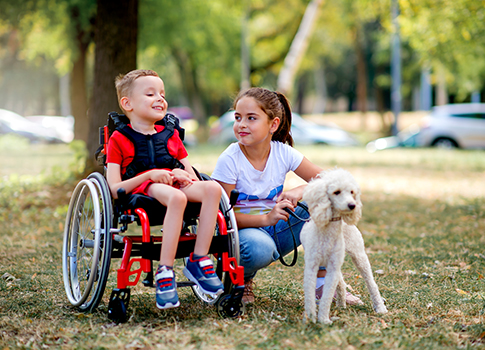 Boy in wheelchair suffering from brain damage and cerebral palsy outdoors next to sister and their dog