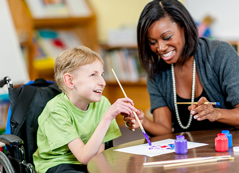 Boy suffering from cerebral palsy smiling while in class with teacher