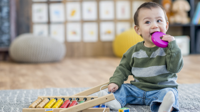 Cure toddler sitting down on rug in living room holding a toy