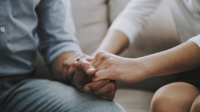Worried couple holding hands while sitting down on sofa