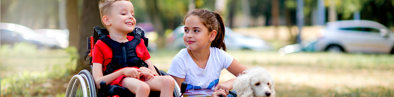 Boy in wheelchair suffering from brain damage and cerebral palsy outdoors next to sister and their dog