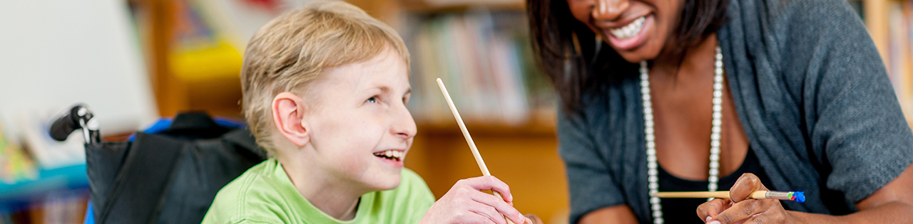Boy suffering from cerebral palsy smiling while in class with teacher