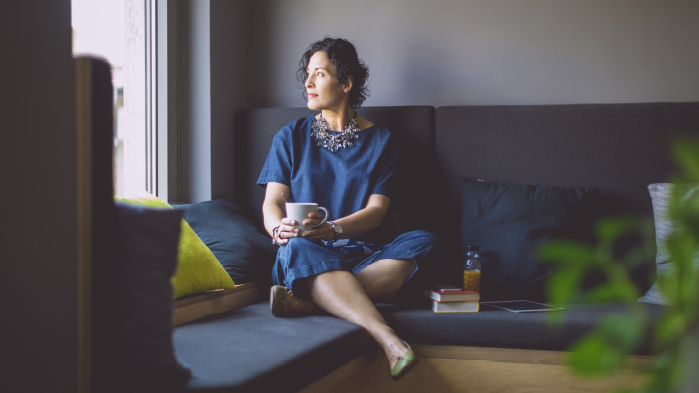 Woman sitting on sofa with mug of tea looking outside sadly after having suffered from sexual abuse
