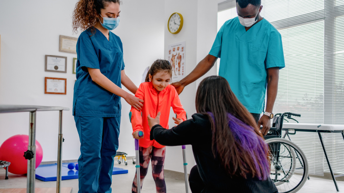 Nurses helping young patient who is suffering from orthopaedic issues to walk