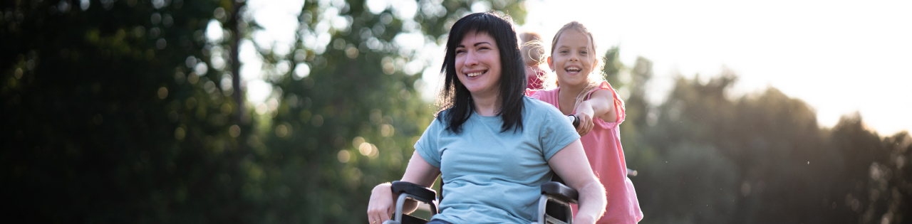 Woman in a wheelchair suffering from spinal injury smiling while her daughter pushes her in the wheelchair
