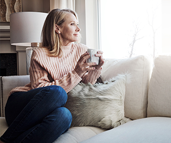 Elderly woman holding a mug of tea sitting in lounge looking outside the window