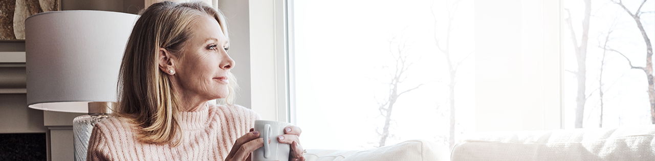 Elderly woman holding a mug of tea sitting in lounge looking outside the window