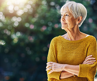 An elderly woman standing outside looking into the distance suffering from Alzheimer's