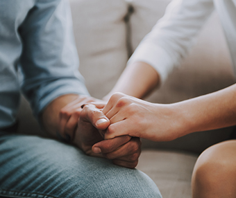 Two people sitting on a couch holding hands